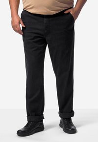 Pantalones de mezclilla negros con un ajuste relajado, que presentan una pierna recta, pockets visibles y puños enrollados, combinados con zapatillas negras.