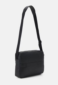 Borsa a tracolla nera con finitura liscia, forma rettangolare, tracolla regolabile e design minimalista senza hardware o dettagli visibili.