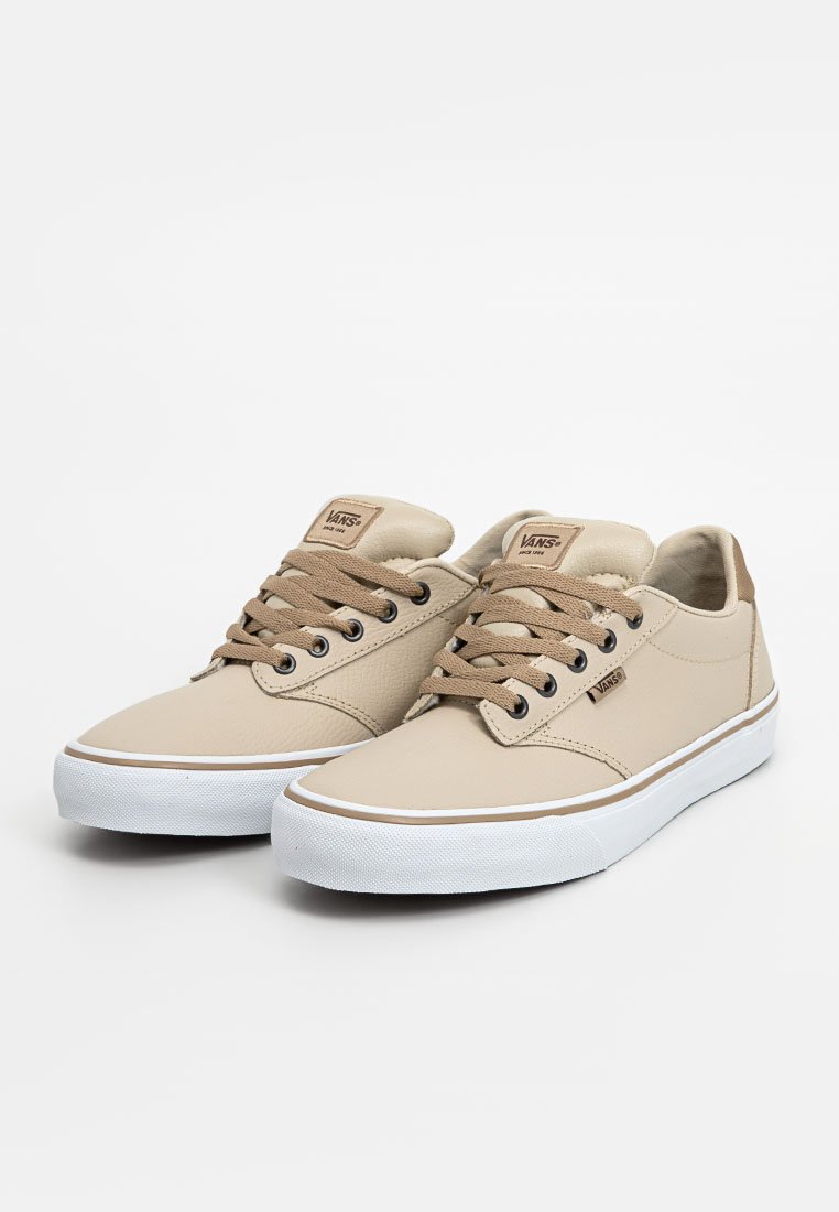 Zapatillas sintéticas beige con un acabado texturizado, cordones marrones, suelas de goma blancas y un acento en el talón color marrón claro. Presenta un logo de Vans en la lengüeta.