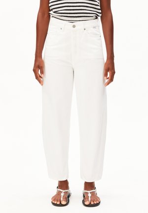 Femme portant un jean blanc droit taille haute, un haut sans manches rayé noir et blanc, et des sandales noires à brides tressées blanches.