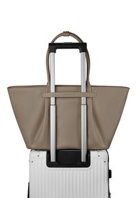 Beige leren tote bag bevestigd aan de verlengde handgreep van een witte harde koffer met wielen.