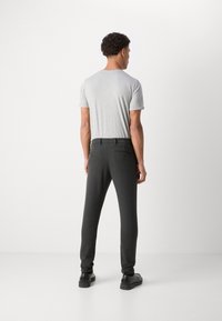 T-shirt gris associé à un pantalon tailleur sombre à coupe slim. Le pantalon est équipé de poches arrière doubles et est porté avec des chaussures noires.