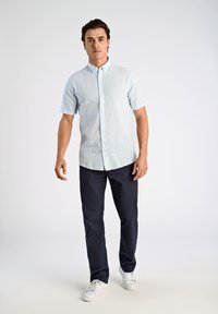 Lichtblauwe shirt met korte mouwen en witte verticale strepen, dichtgeknoopt, gecombineerd met donkerblauwe broek en witte sneakers. Eenvoudig ontwerp, casual pasvorm.
