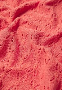 Tissu texturé corail présentant des motifs découpés complexes, un design en vagues et un aspect doux et froissé. Idéal pour les vêtements ou les accessoires.