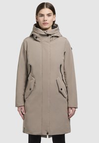Beige lange jas met een capuchon, voorzien van ritszakken, drukknoopsluiting en een gladde textuur. Ontworpen voor warmte en bescherming tegen de elementen.