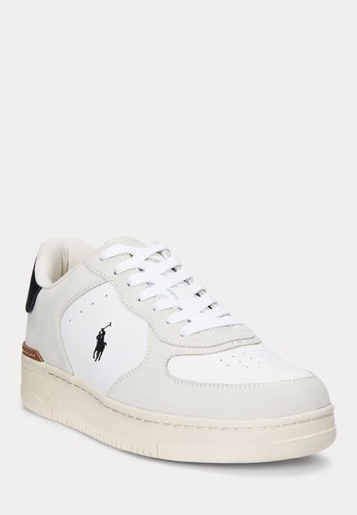 Bijela niska tenisica s bež obrubom, vezicama sprijeda, crnim logom sa strane i crnom petnom trakom.