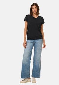 T-shirt nera a V, tessuto morbido, vestibilità comoda; abbinata a jeans a gamba larga di colore blu chiaro; completata con sneakers chiare con dettagli verdi.