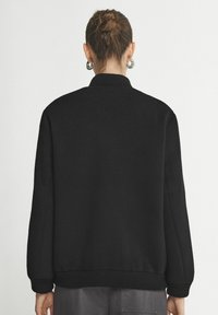 Svart sweatshirt med rund halsringning, ribbade ärmslut och nederkant, med en slät textur och avslappnad passform, sedd bakifrån.