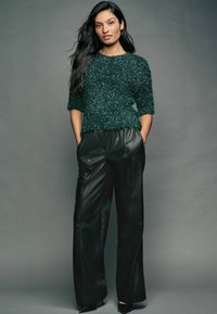 Maglione textured verde scuro con maniche corte, abbinato a pantaloni in pelle nera a gamba larga. L'outfit presenta una silhouette rilassata e accenti minimali.