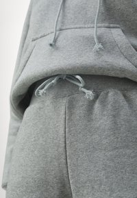 Grå sweatshirt och sweatpants-set, tillverkat av mjukt tyg, med en framsida ficka, dragsko i midjan och ribbad nederkant och ärmslut.