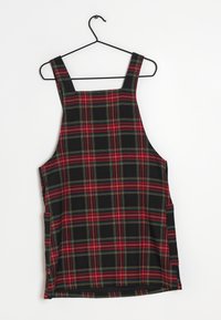 Schwarzes karierter Latzkleid mit roten und grünen Linien, ausgestattet mit breiten Schulterträgern und seitlichen Taschen. Das Material ist weich und elastisch.