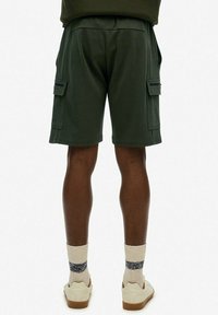 Oliwkowe szorty cargo z dwoma kieszeniami bocznymi, wykonane z miękkiego materiału. Stylizowane z neutralnymi sneakersami i jasnymi skarpetkami prążkowymi.