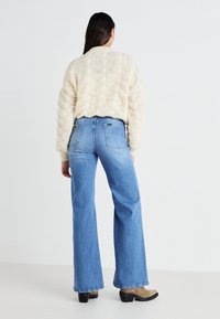 Maglione cremoso a maglia testurizzata con scollo a barca e vestibilità ampia, abbinato a jeans svasati azzurro chiaro con tasche posteriori e dettagli di cucitura.