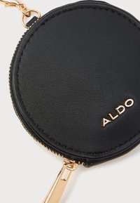 Čierny kožený okrúhly púzdro na mince so zlatým zipsom a kovovými prvkami, s embosovaným logom "ALDO" na prednej strane. Textúrovaný povrch.