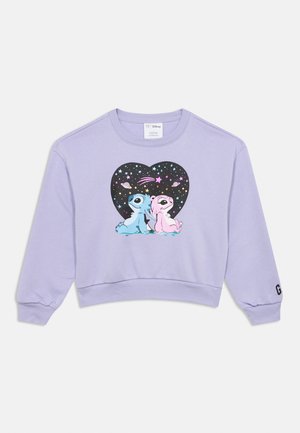 Lavandas krāsas cropped džemperis ar grafisku attēlu, kurā redzami divi zīmējumu tēli melna sirds priekšplānā ar krāsainām zvaigznēm un planētām.