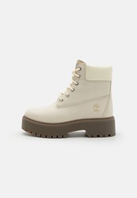 Beige waterproof ankle boot with a textured surface, round toe, lace-up front, silver eyelets, and chunky brown rubber sole.