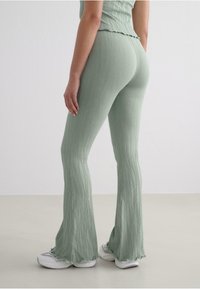 Light green ribbed flared pants with a textured finish, featuring a wavy hemline, paired with white sneakers.