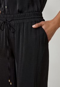 Zwarte jumpsuit met een geraffineerde tailleband, verstelbare trekkoord, zijzakken en een soepele, licht glanzende stoftextuur.