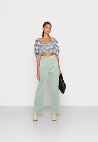 Top cropped em preto e branco com padrão xadrez e mangas bufantes, emparelhado com calças de veludo cotelê largas em verde menta e uma bolsa preta. Botas de tornozelo bege.