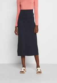 Gonna midi blu navy in tessuto morbido, con vita aderente. Abbinata a una maglia a maniche lunghe rosa chiaro e sandali beige.