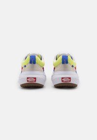 Bakside av flerfargede Vans-sneakers med en hvit gummisåle, gule accenter og teksturert beige materiale på overdelen. Rødt merke på hælen.
