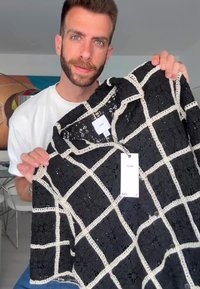 Camisa de encaje negro con un patrón de cuadrícula en blanco, mangas cortas y cuello. Etiquetas visibles con información de talla y cuidado.