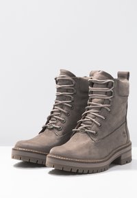 Grå läderstövlar med texturerad finish, gummisulor och metallöglor. Har vadderad krage och snörningsdesign. Platt, robust konstruktion.