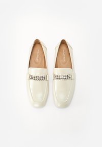 Ljusbeige loafers gjorda av släta läder, med ett dekorativt band av strass över ovandelen och en platt sula.