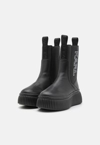 Bottines noires en cuir avec des panneaux élastiques sur les côtés et une semelle à plateforme nervurée. Marque "KARL" en cristaux sur le côté extérieur.