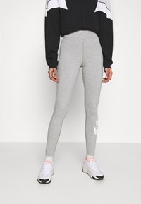 Szürke pamut leggings, slim fit fazonnal, a bal lábon fehér Nike logóval. Fekete-fehér cropped pulóverrel és sportcipővel párosítva.