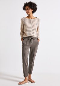 Maglione beige a maglia con motivo a zigzag, abbinato a pantaloni jogger grigi, tapered, con cordoncino e piping laterale. Sandali piatti completano il look.
