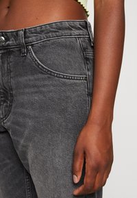 Czarne dżinsy z wysokim stanem, pięcioma kieszeniami i subtelnymi detalami w przeszyciach. Materiał ma gładkie, lekko teksturowane wykończenie.