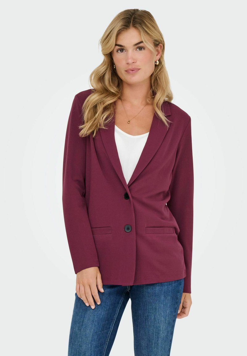 Mava žakete ar garām piedurknēm, vienu pogu slēgšanu un divām priekšējām kabatām. Savienota ar baltu topi un zilām džinsām. Gluda auduma tekstūra.