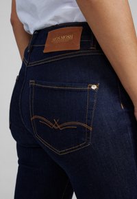 Pantalones vaqueros de mezclilla azul oscura con costuras naranjas, que cuentan con una etiqueta de cuero en la cinturilla y un diseño sutil en los bolsillos traseros.