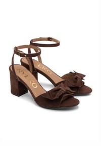 Sandali con tacco alto in suede marrone, con punta aperta, cinturino alla caviglia e un fiocco decorativo sulla parte anteriore. Tacco a blocco quadrato.