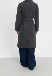 Šedý vlněný kabát s páskem v oblasti pasu, dlouhými rukávy a límcem. Kabát sahá k polovici lýtek a je spárován s širokými modrými džíny.