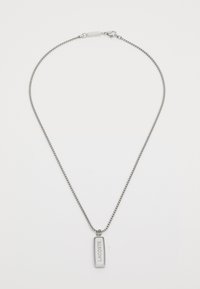 Collier en argent avec un pendentif rectangulaire gravé "LACOSTE". La chaîne est finement maillée et le pendentif présente un fini lisse.