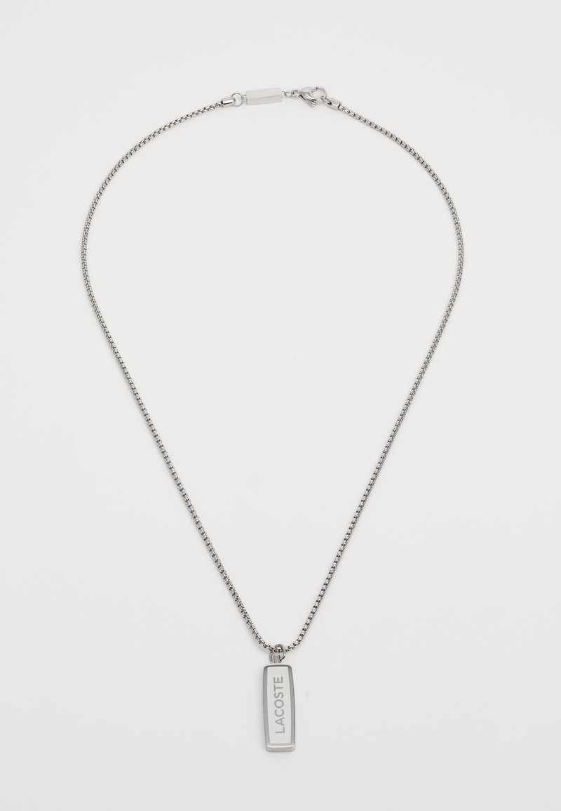 Collier en argent avec un pendentif rectangulaire gravé "LACOSTE". La chaîne est finement maillée et le pendentif présente un fini lisse.