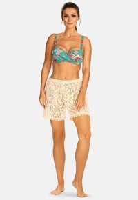 Turkusowy top od bikini w kwiatowy wzór z szerokimi ramiączkami, zestawiony z jasnobeżowymi koronkowymi szortami z falowanymi brzegami i misternymi wzorami.