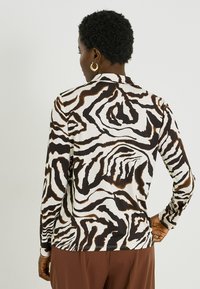 Camisa de manga larga confeccionada en tejido ligero, con un patrón abstracto de cebra en blanco y negro con detalles en marrón, diseñada con cuello.