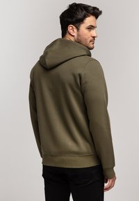 Oliwkowa bluza z kapturem z miękkiego materiału, z sznurkiem do regulacji, ściągaczami przy rękawach i u dołu oraz gładkim, lekko teksturowanym wykończeniem.