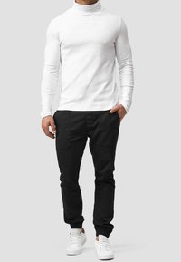 Valkoinen pitkähihaisuus turtleneck, istuva malli, yhdistetty mustiin jogger-housuihin, joustavat hihansuut ja valkoiset tennarit. Yksinkertainen ja moderni ilme.