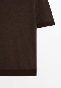 Haut à manches courtes marron côtelé avec un ourlet contrastant marron foncé. Il présente un matériau tricoté texturé et un design simple et contemporain.