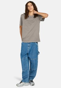 Szara koszulka z krótkim rękawem połączona z luźnymi niebieskimi spodniami cargo z denimu. Strój charakteryzuje się swobodnym krojem i fakturowaną tkaniną. Srebrne buty sportowe.