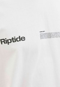 Hvid bomulds t-shirt med et markant sort "Riptide" logo og bloktekst på venstre side, med yderligere tekst nedenfor. Enkel design.