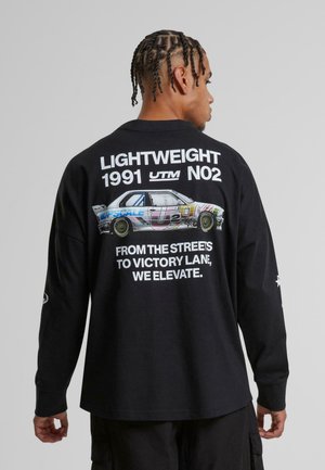 Black long-sleeve shirt featuring a car graphic and white text on the back. Text includes “LIGHTWEIGHT 1991 UTM NO2” and a slogan below.
