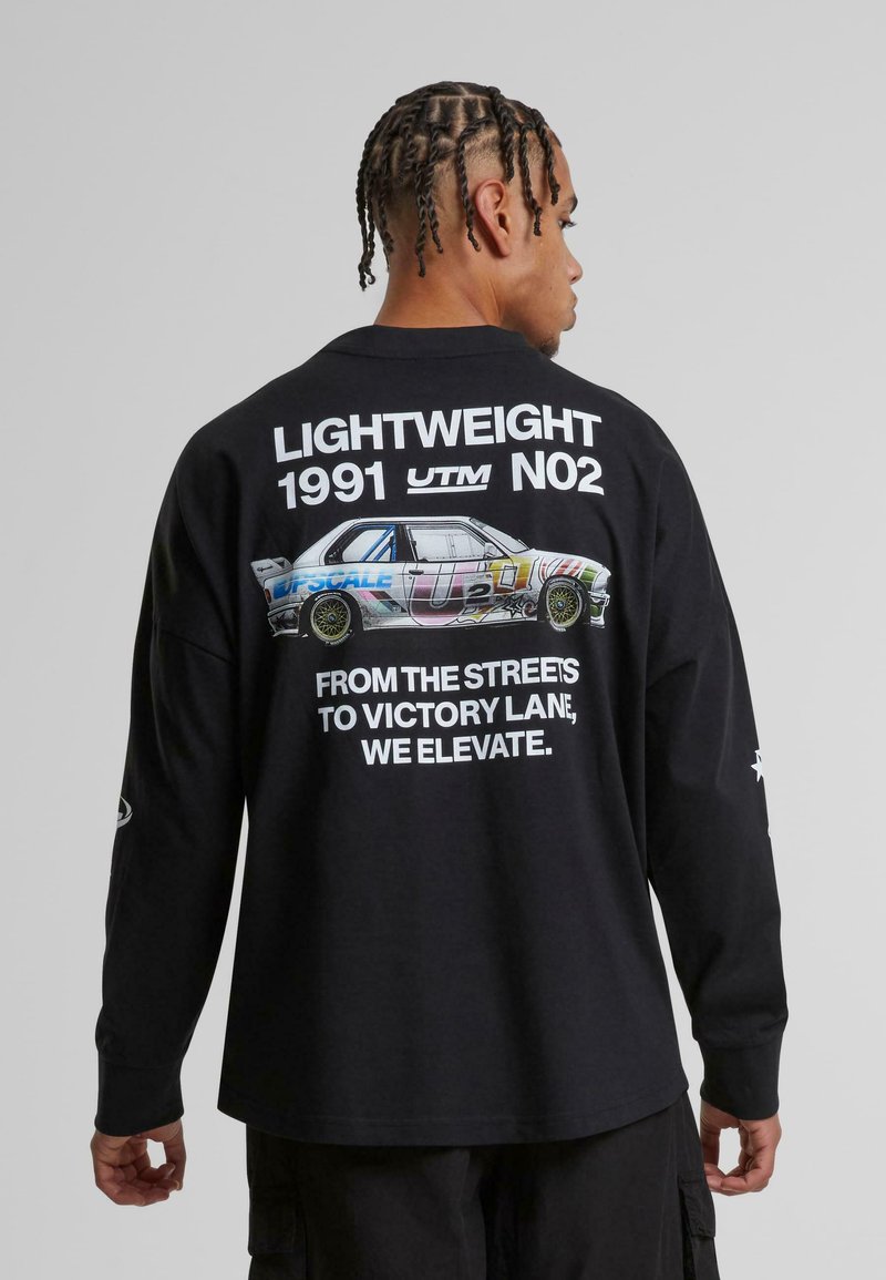 Juodas ilgarankovis marškinėliai su automobilių grafika ir balta tekstu nugaroje. Tekste yra "LIGHTWEIGHT 1991 UTM NO2" ir po juo esanti šūkis.