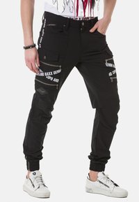 Schwarze Jogginghosen mit Reißverschlusstaschen, elastischen Bündchen und Textdetails mit Logo. Hergestellt aus strapazierfähigem Material mit glatter Textur.