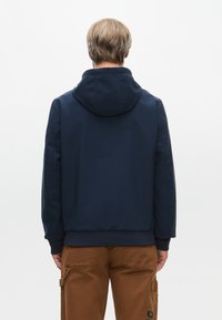 Marineblå hættejakke lavet af glat, vandafvisende stof med ribbede manchetter og kant. Høj krave og minimale syninger forbedrer designet.