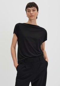 Top nero a maniche corte con una vestibilità morbida e scollo rotondo, realizzato in un tessuto liscio e leggero; abbinato a pantaloni neri sartoriali.